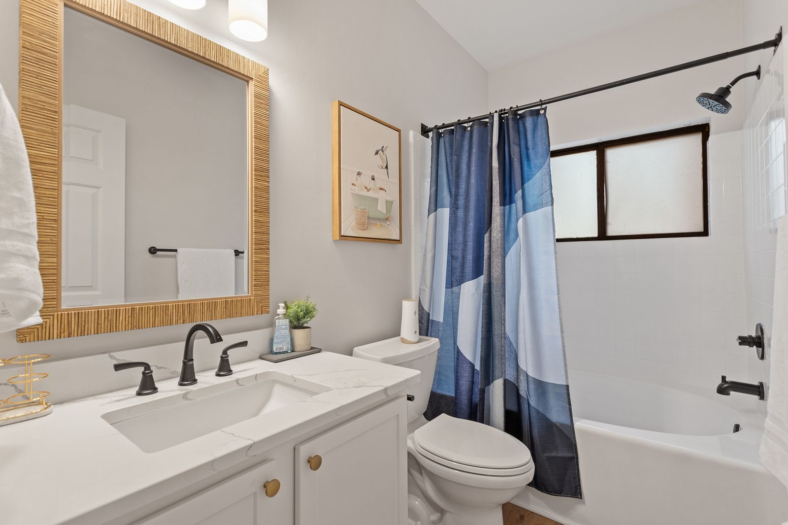 Bathroom with quartz vanity, rattan mirror and tub with shower