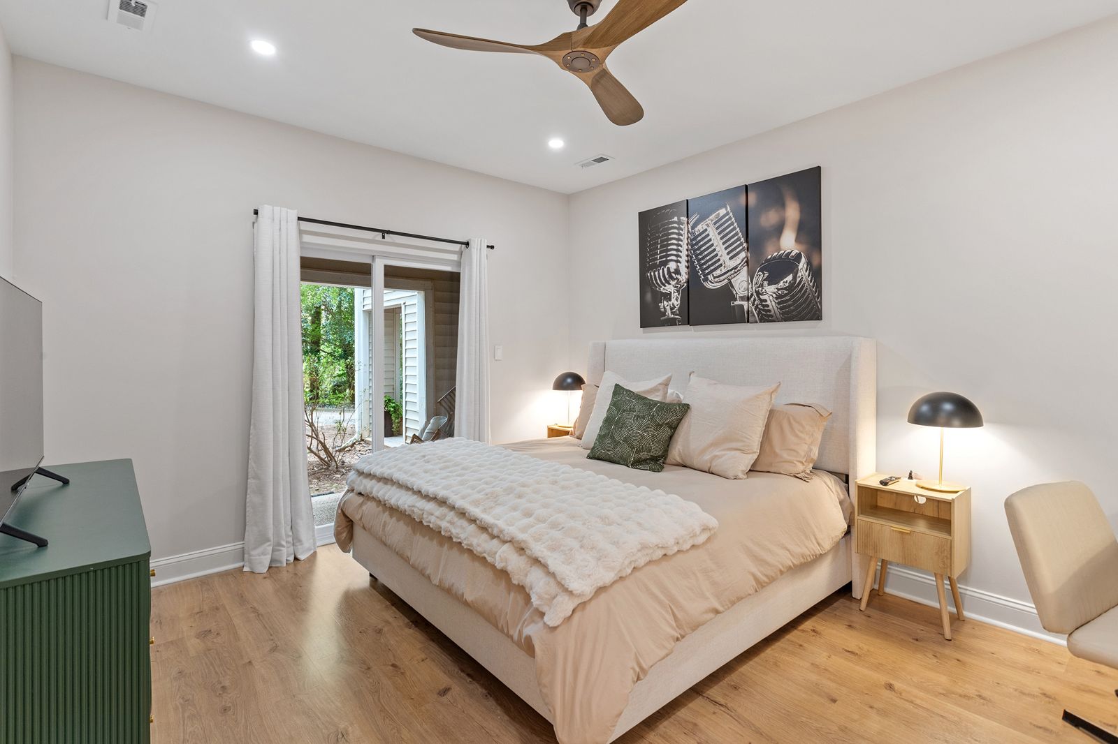 Primary bedroom with an upholstered king bed, lamps on both sides and a sliding door to the patio